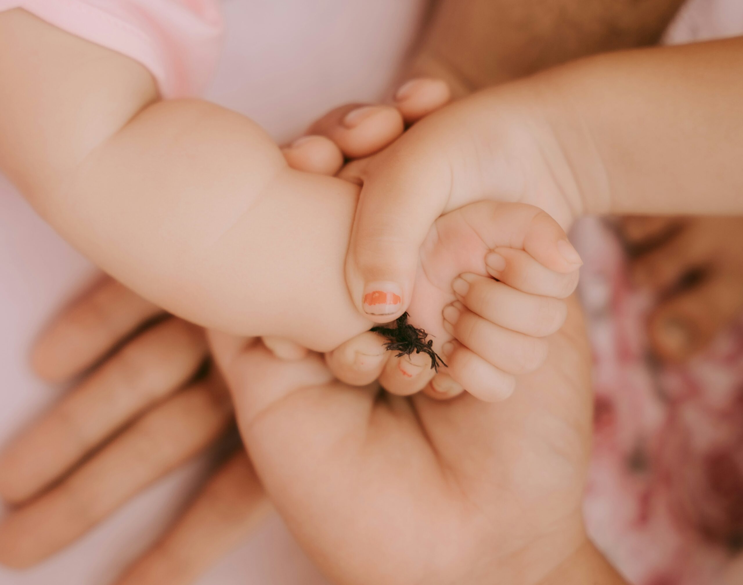 A parent carefully trimming a smiling toddler's nails while another child plays nearby.