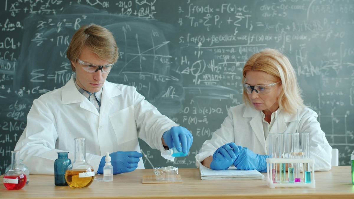 Man and woman scientists are busy with chemistry experiment in classroom pouring liquid substances in test tube. People, education and science concept.