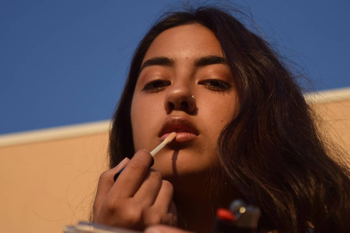 Young brunette woman applying lip gloss